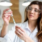 female scientist with safety glasses holding syringe with vaccine lab 1